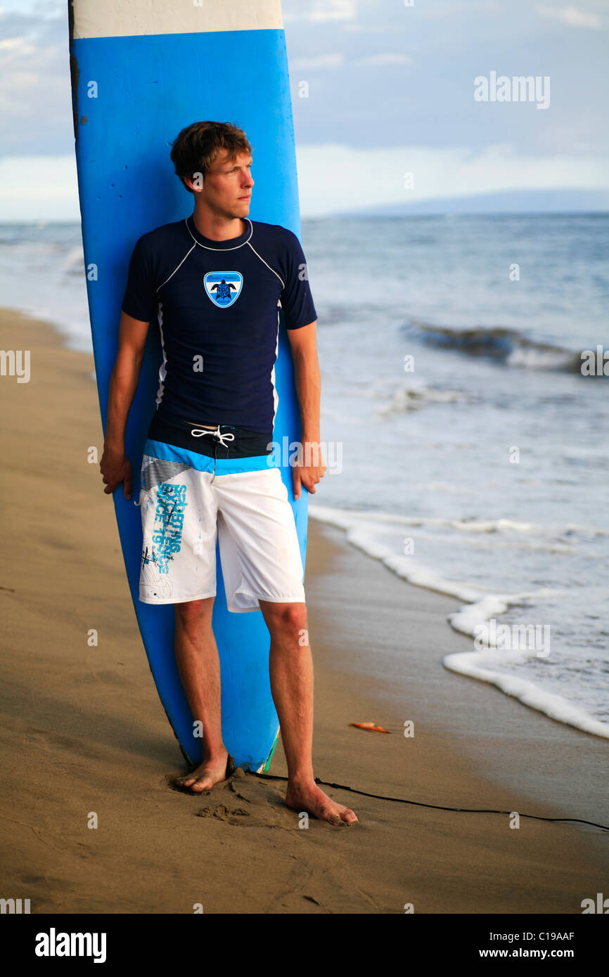 Surfer wearing boardshorts and surfshirt standing in front of his ...