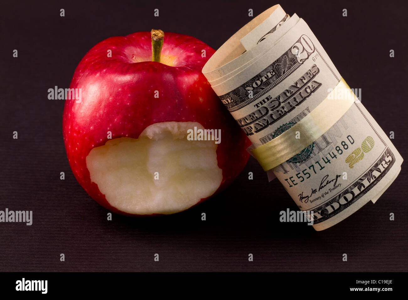 American currency leans against a red apple with a bite taken out to reflect the recession's weakened consumer. Stock Photo