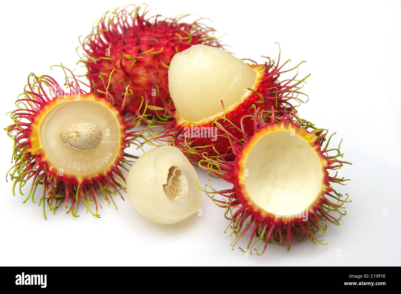 Hairy, red Rambutan fruit (Nephelium lappaceum). Whole fruits, some peeled, showing white edible flesh and seed. Shot on white. Stock Photo