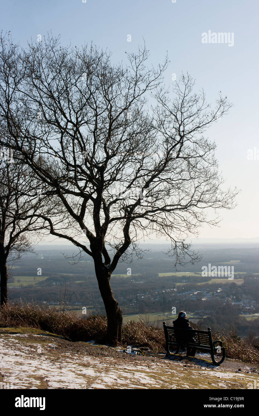 Walker on seat on top of Pitch Hill near Ewhurst Surrey in Winter, taking in the view toward the South Downs Stock Photo