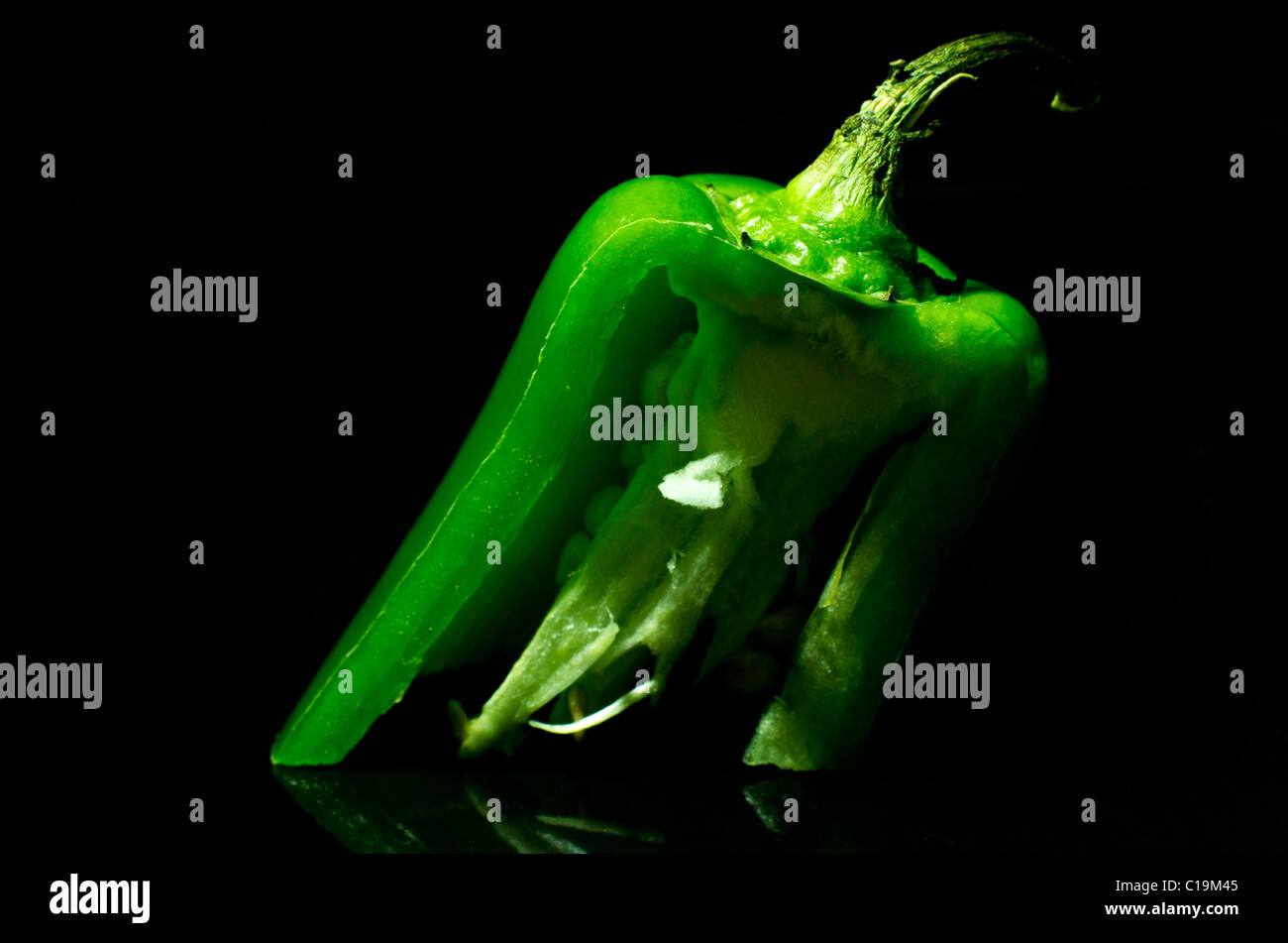 A cross-section of a jalapeno pepper, cut at an odd angle and balanced upright on a black reflective plate. Stock Photo