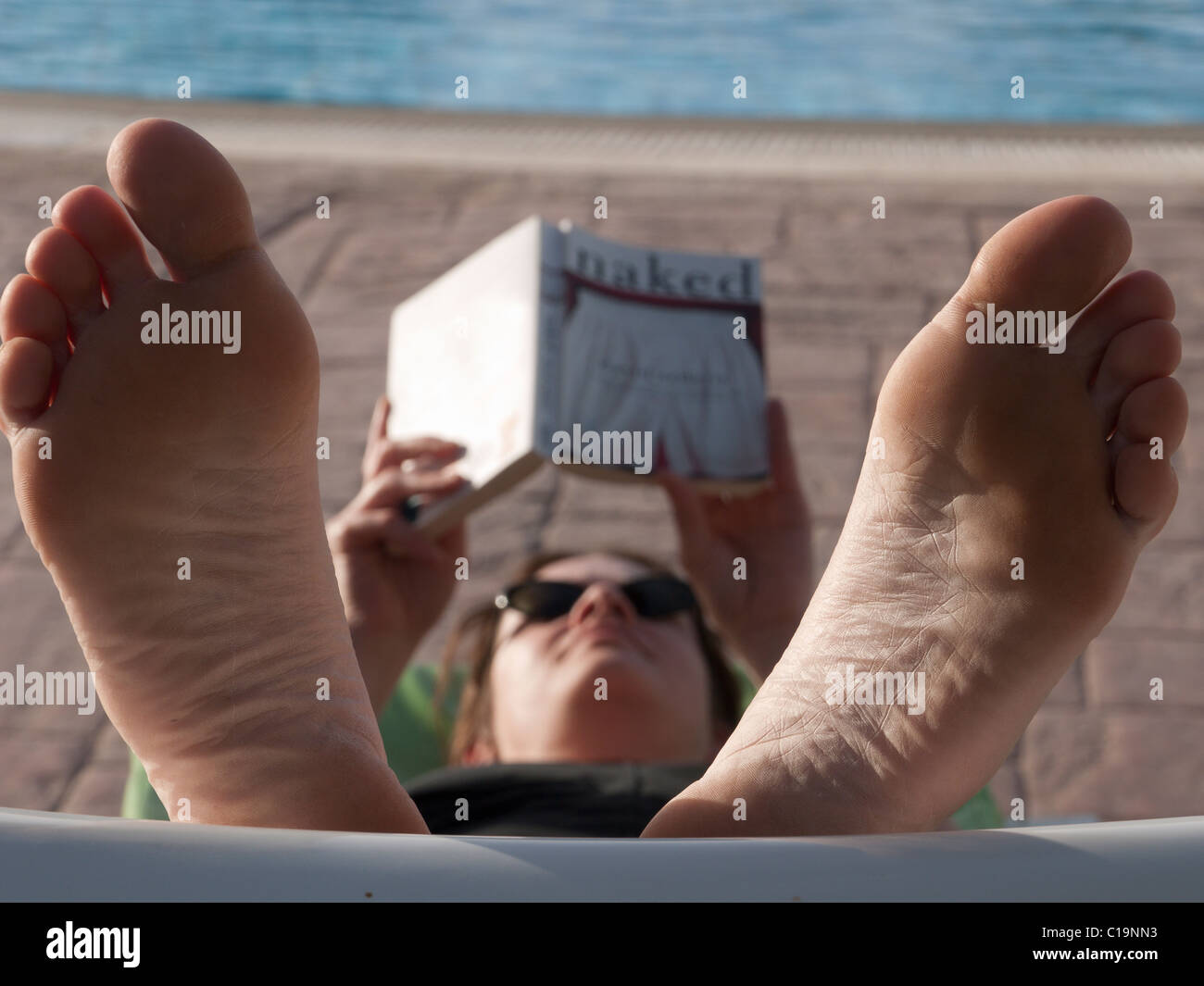 A Young Woman With Feet Up Relaxes By Reading Beside Swi A Young Woman With Feet Up Relaxes By Reading Beside Swi