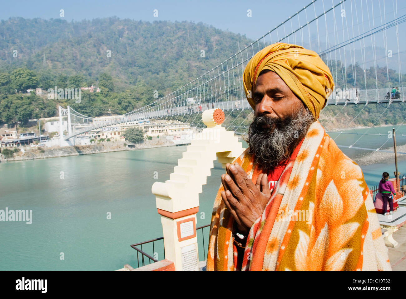 Sadhu praying with Lakshman Jhula in the background, Ganges River, Rishikesh, Uttarakhand, India Stock Photo