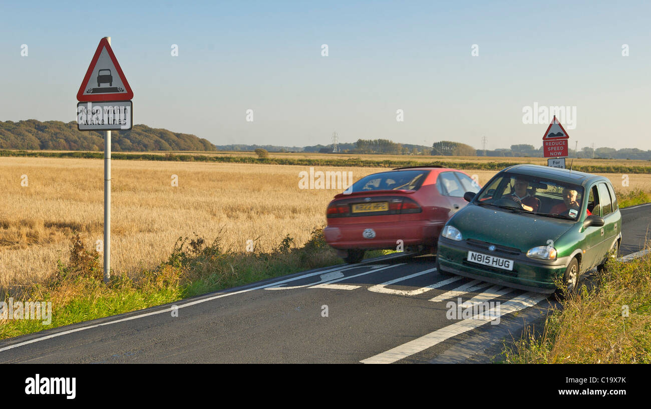 Two cars squeezing past at speed over painted slow sign on a very narrow country road Stock Photo