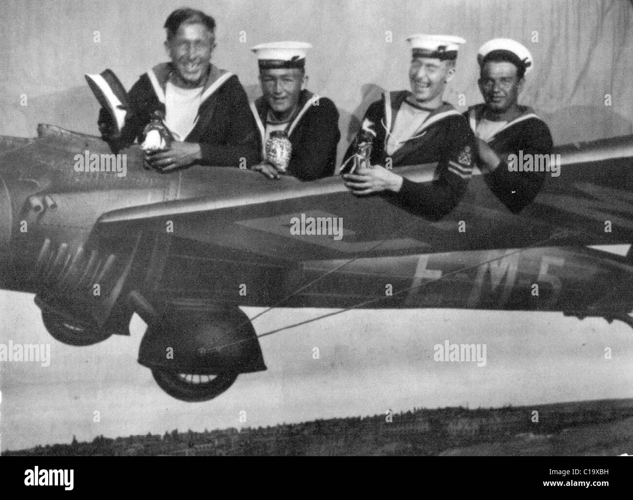 Four British Royal Navy sailors on shore leave pose in model aeroplane thought to be from HMS Adventure around 1936-37 Stock Photo