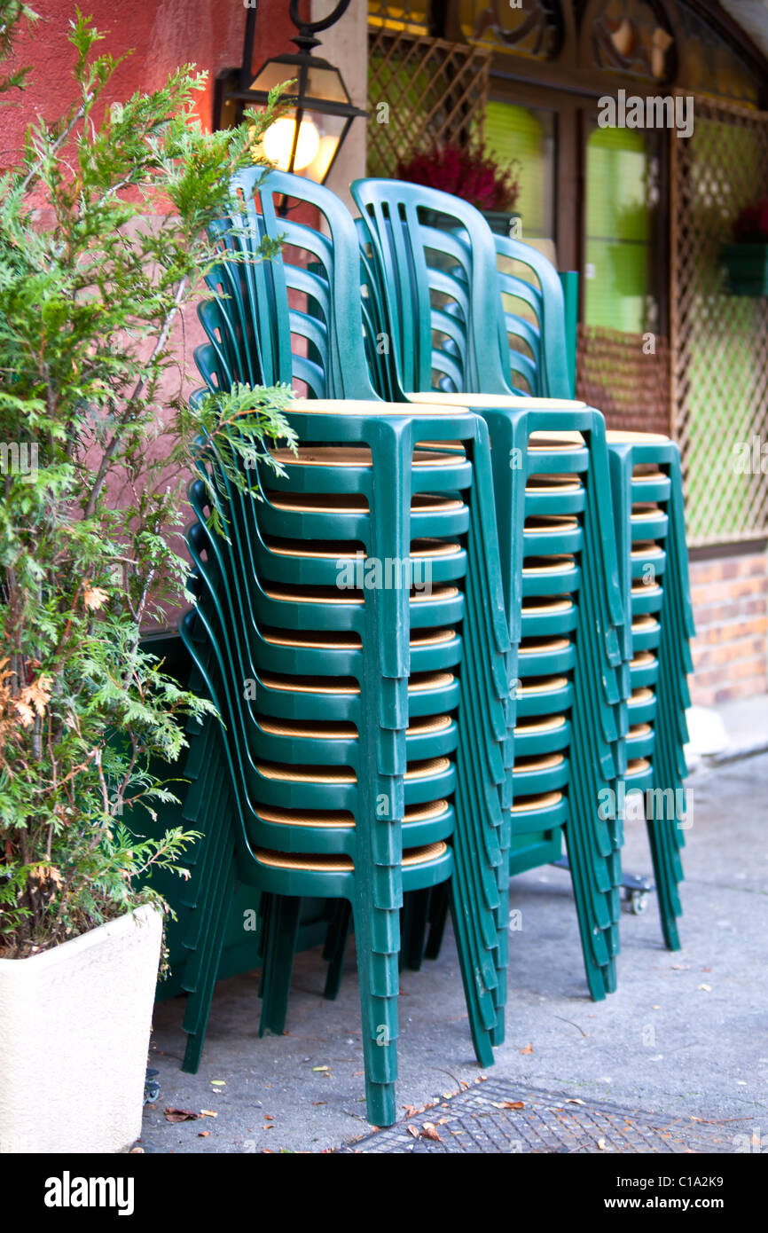 pile of green plastic chairs against the cafe wall on a street Stock