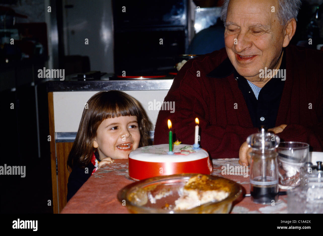 Childs Birthday Party Child Looking At Cake Next To Grandfather Stock Photo