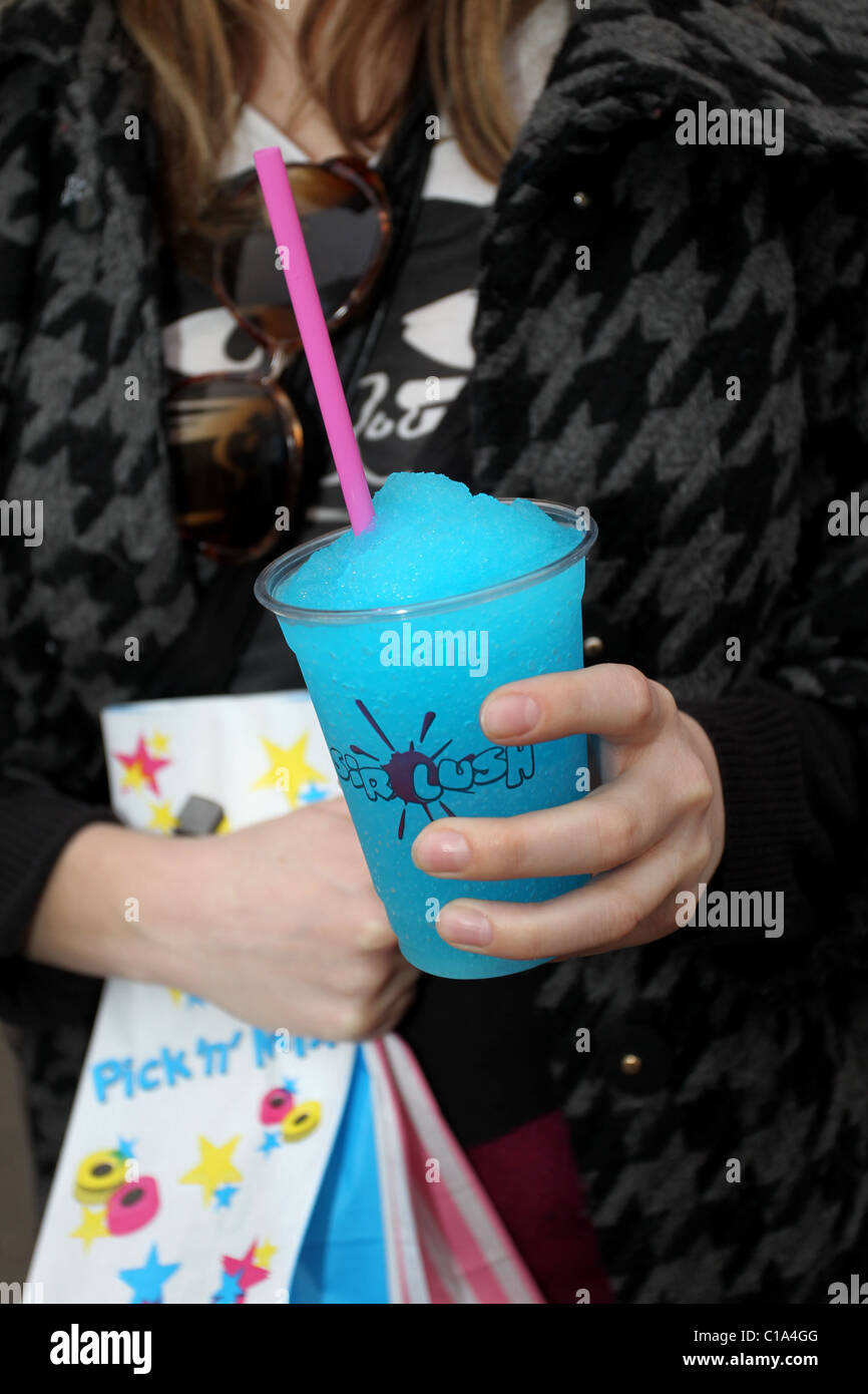 A girl pictured drinking a slush puppy with bags of sweets outside a sweet shop in Worthing, West Sussex, UK. Stock Photo