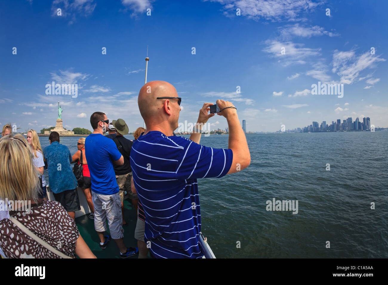 Tourists cruise by Statue of Liberty in New York Harbor taking pictures of Manhattan skyline. Stock Photo
