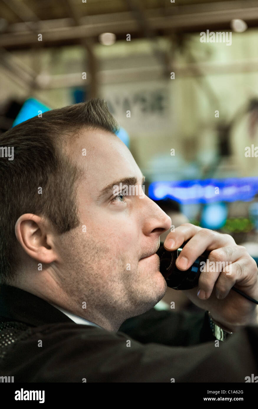 A Securities Trader consults the market-data screens around him while calling in a order. Stock Photo