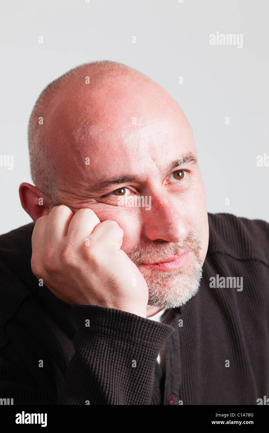 UK, Europe. Bald headed mature man resting his chin on his hand with a bored facial expression Stock Photo