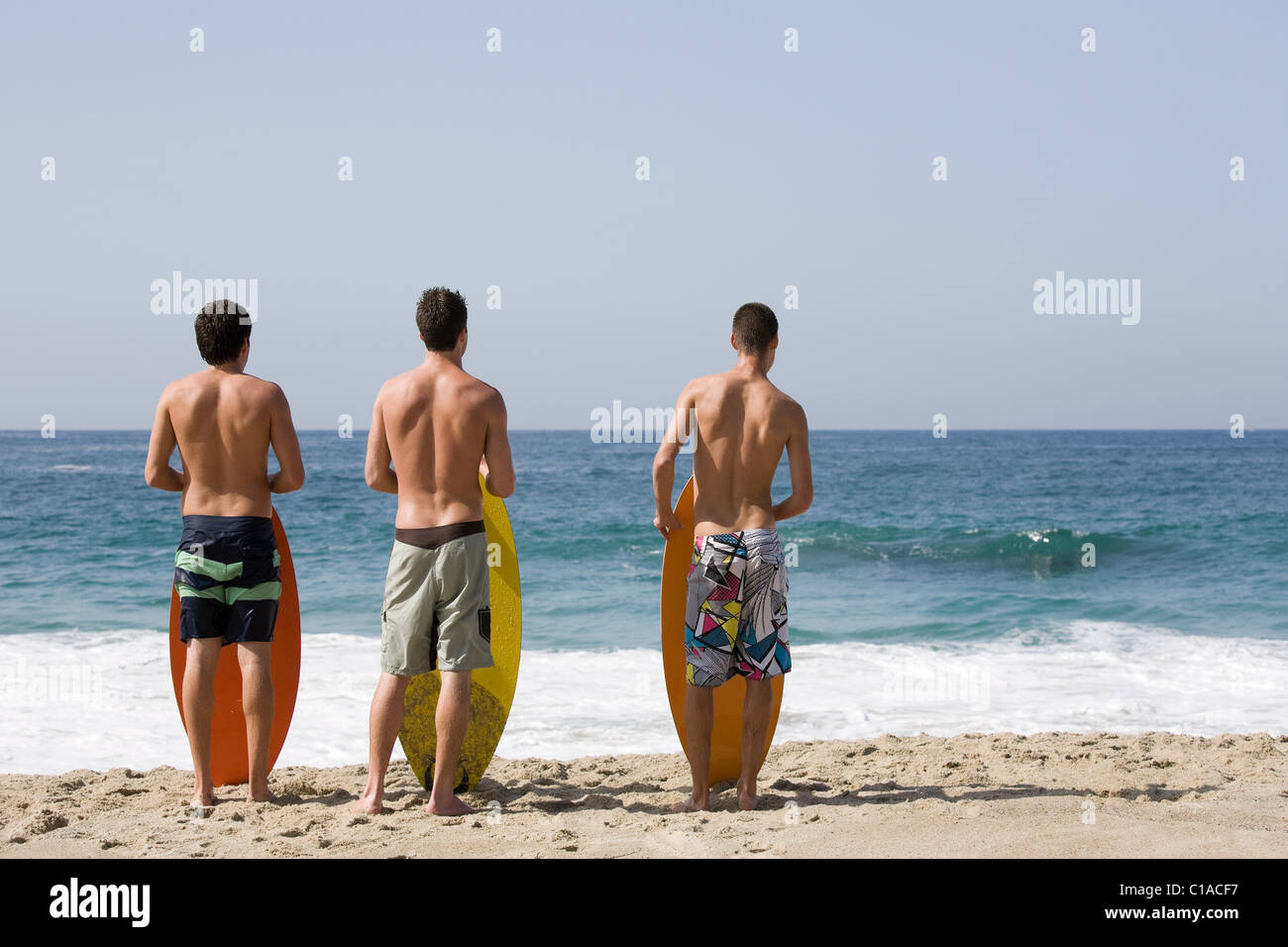 Three young men on beach with surfboards Stock Photo