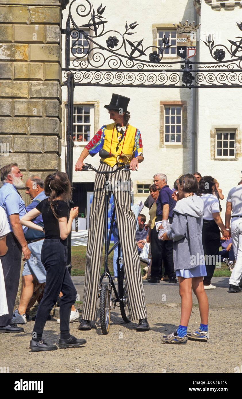 Clown on stilts riding bicycle at gates, Traquair Fair Stock Photo Alamy