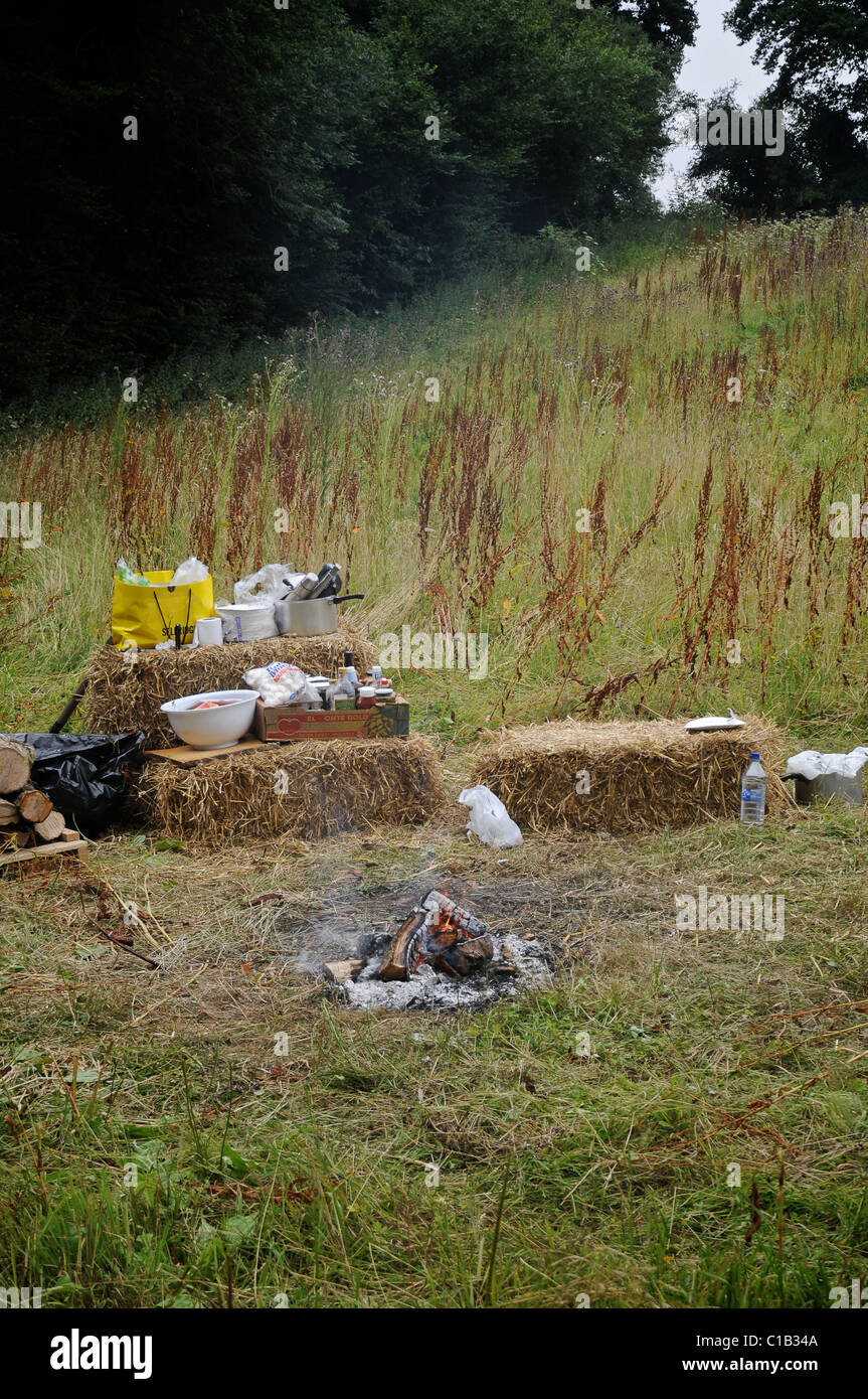 Camping outdoors in a field. Campfire in the center with logs and hay bales all around. Outdoors in a field of wild grass. Stock Photo
