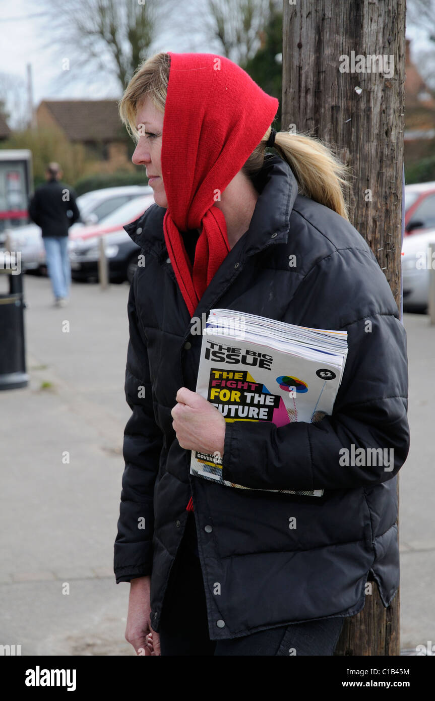 Woman standing in the street selling copies of the Big Issue a publication to help the unemployed to make a living Stock Photo