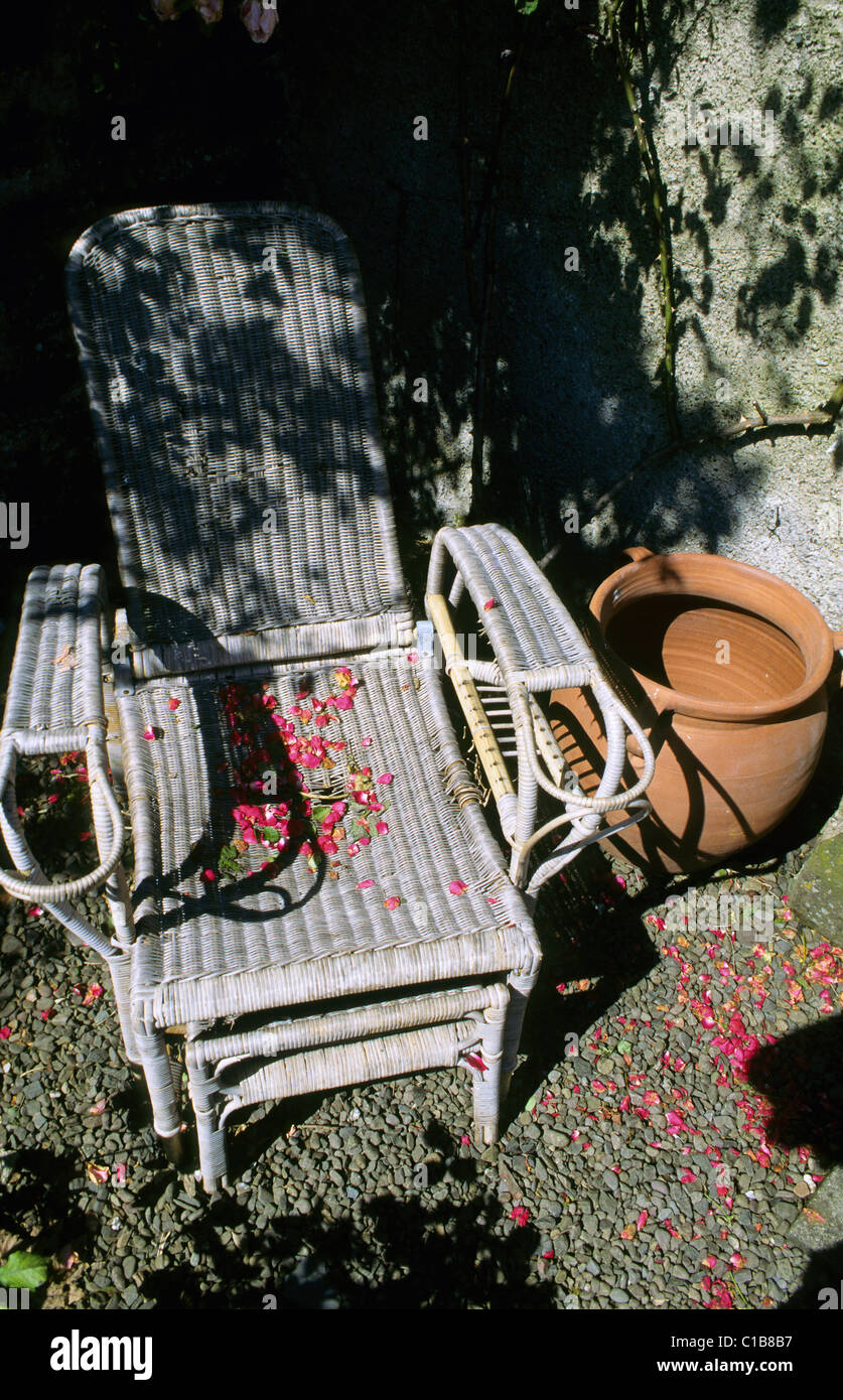 Rose petals fallen gracefully upon faded weathered garden whicker seat Stock Photo