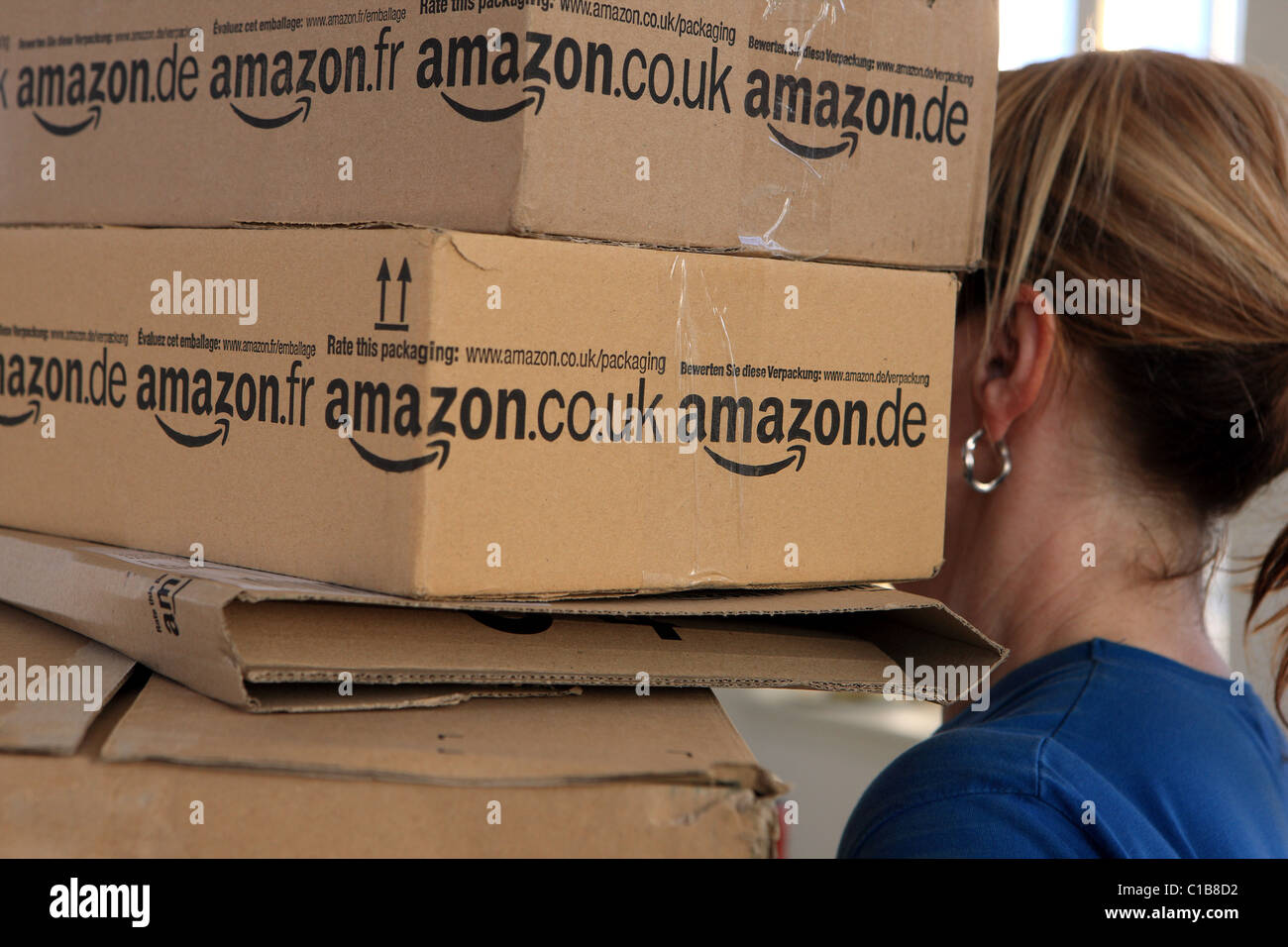 Woman carrying a stack of Amazon boxes Stock Photo