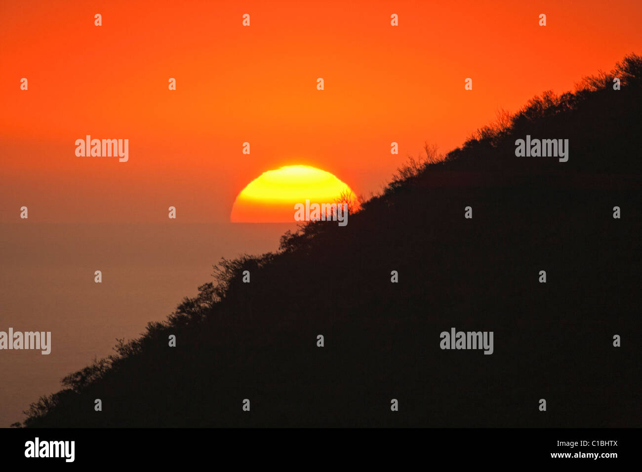 Giant sun ball sets behind pali (cliff) of Kealakekua Bay in South Kona, Hawaii Stock Photo