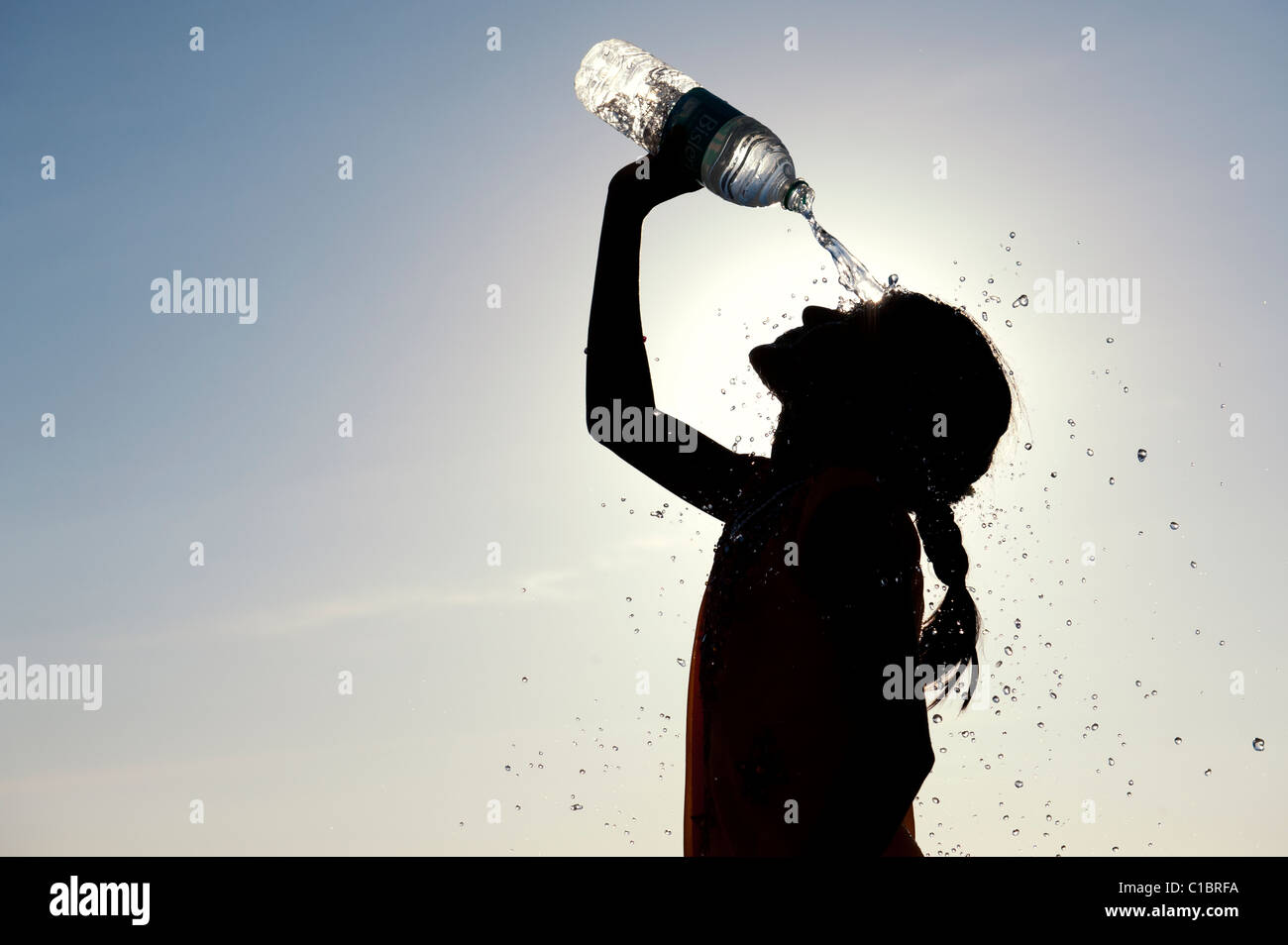 Indian girl cooling off with bottled water. India.  Silhouette Stock Photo