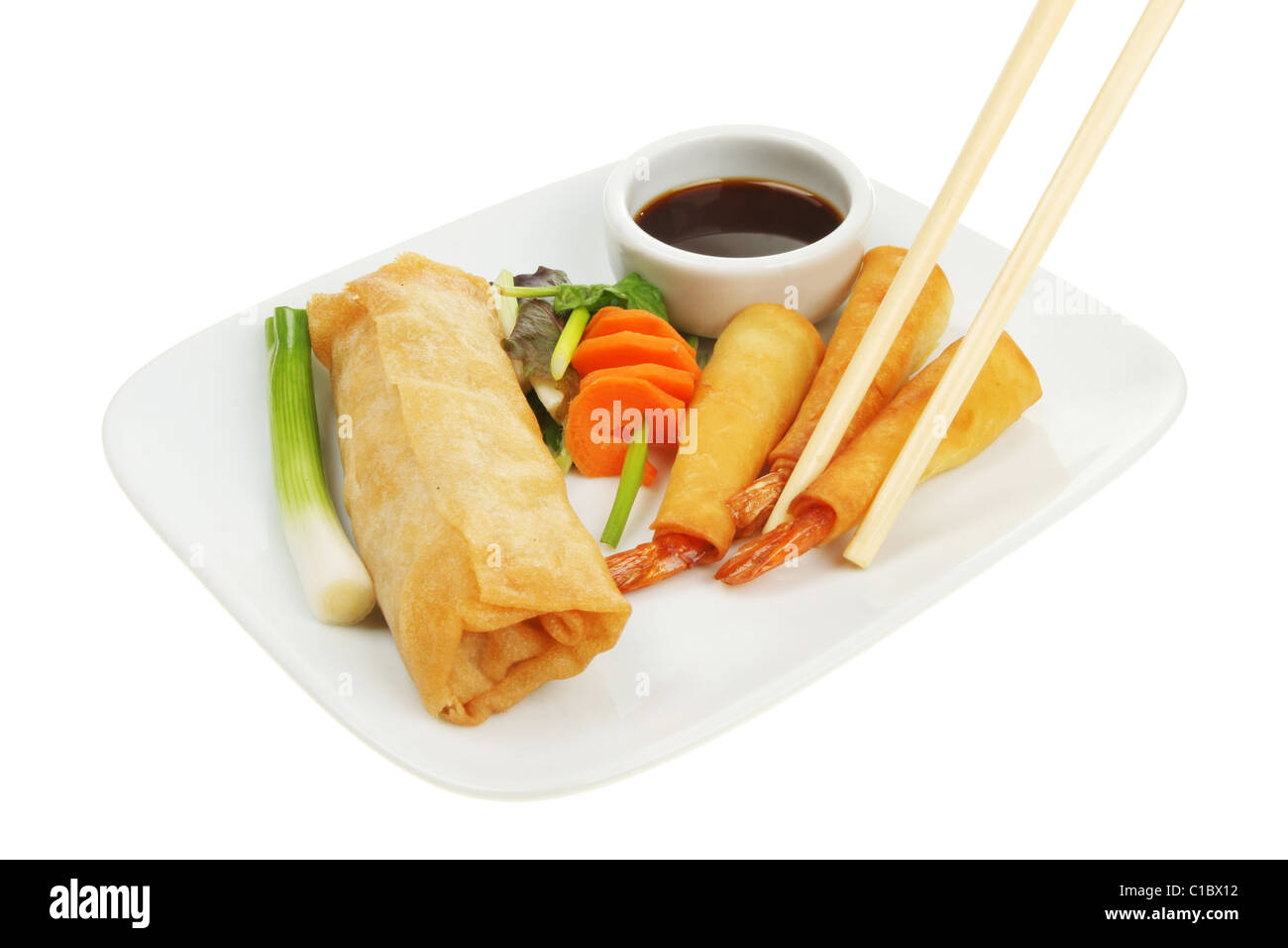 Chopsticks picking a wrapped prawn from a plate of Chinese food Stock Photo