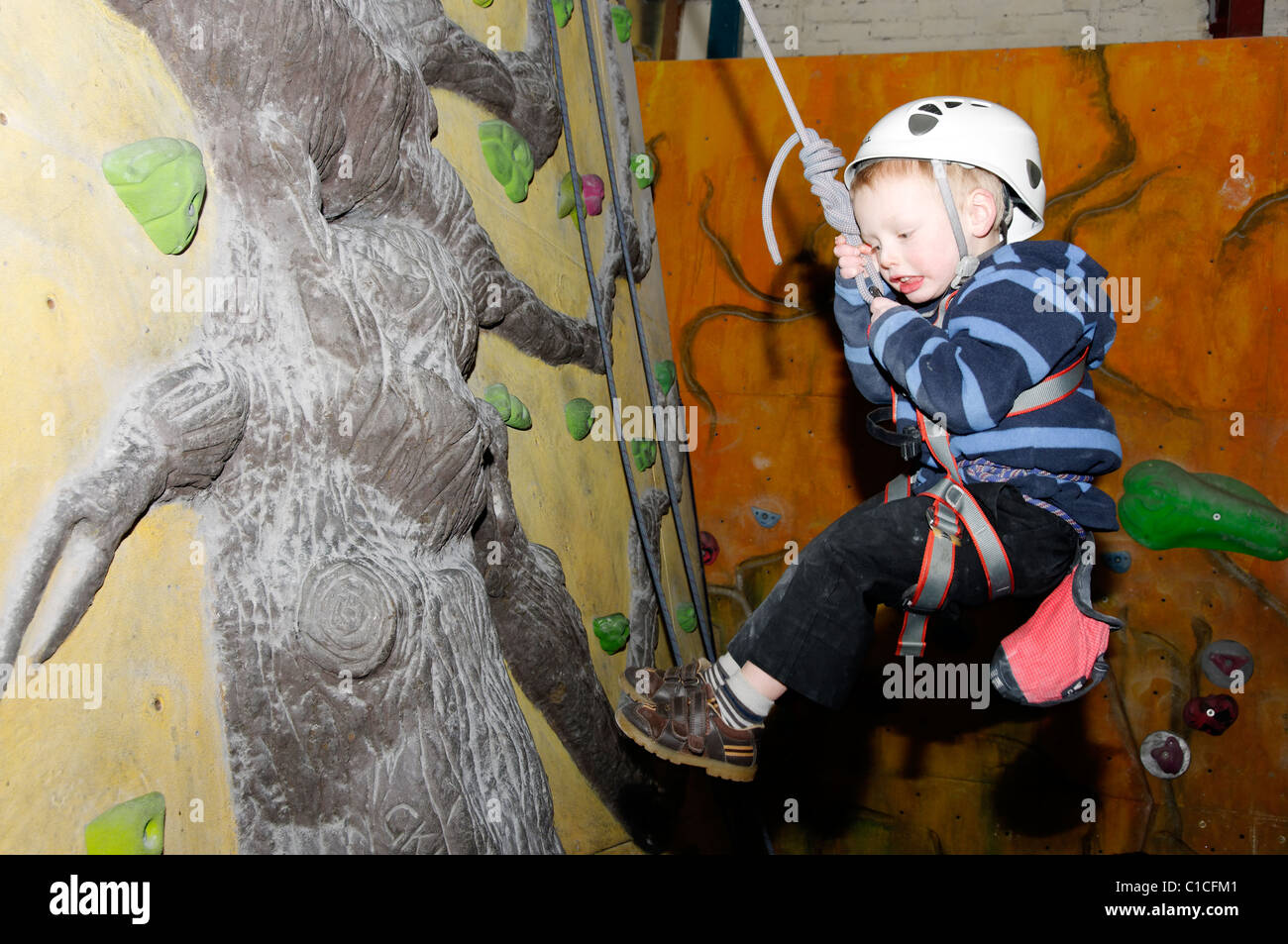 A young boy swinging on a rope at an indoor climbing wall Stock Photo