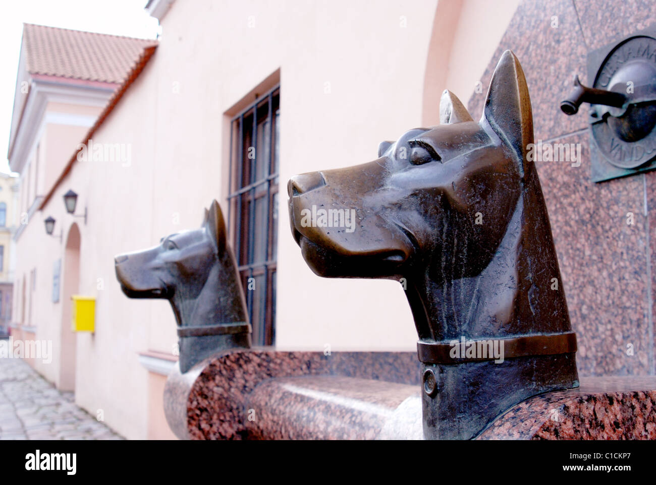 Sculptures Of Two Metal Dog Heads Near The Water Tap In The Street 