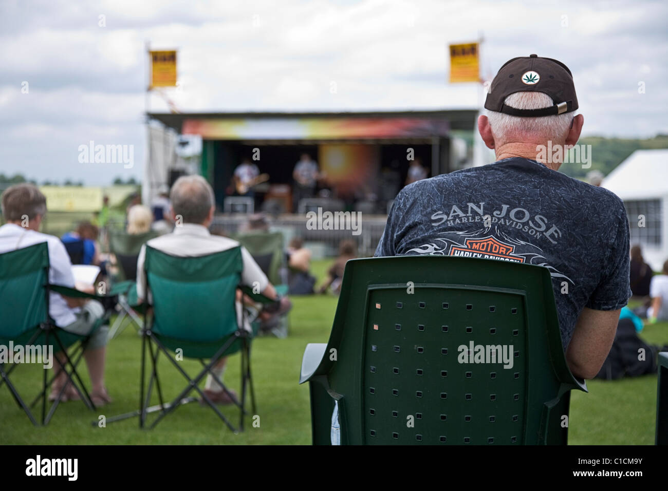 A mature male music fan wearing a baseball cap and Harley Davidson tee shirt enjoying the music at an outdoor music festival Stock Photo