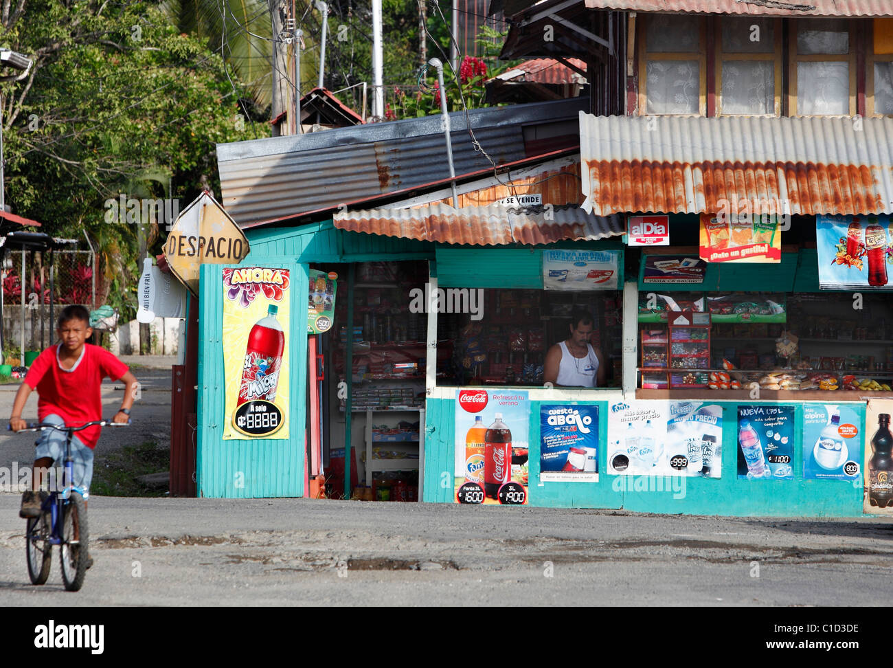 A boy rides his bicycle past a neighborhood grocery store, Quepos, Costa Rica Stock Photo