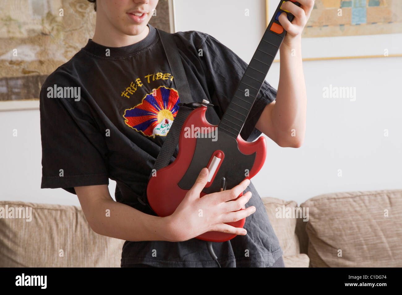 A teenage boy playing the Playstation game Guitar Hero wearing a Free  Tibet-T-shirt Stock Photo - Alamy