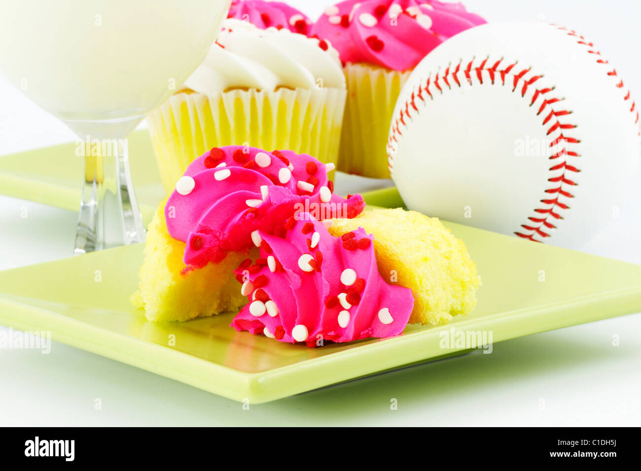 Vanilla cupcakes with pink icing, white milk, and a baseball suggest a festive, after game celebration. Stock Photo