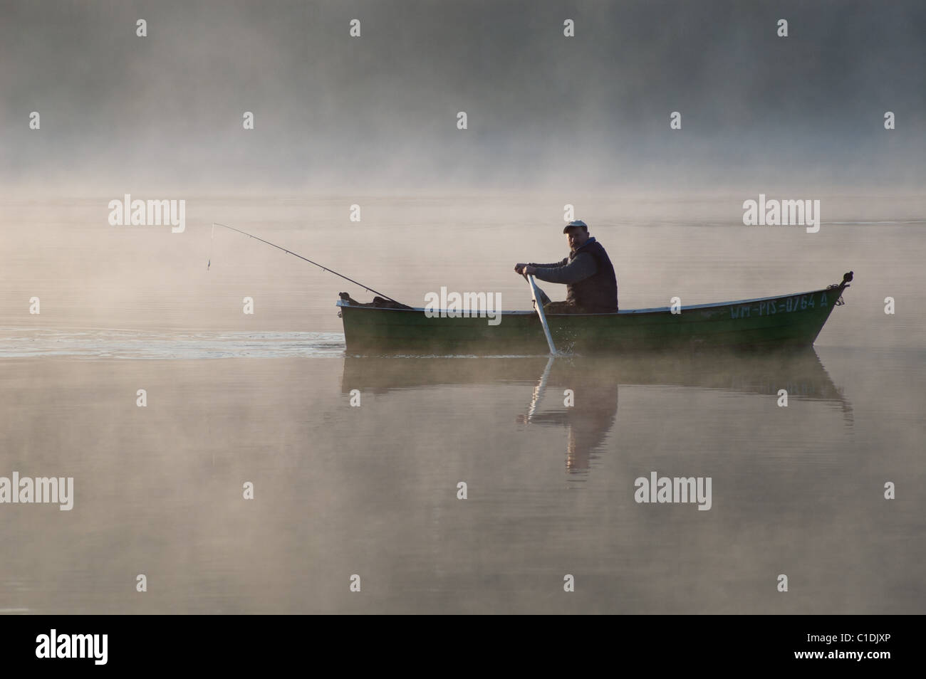 Angler in his boat, rowing through foggy lake. Masuria, Poland Stock Photo
