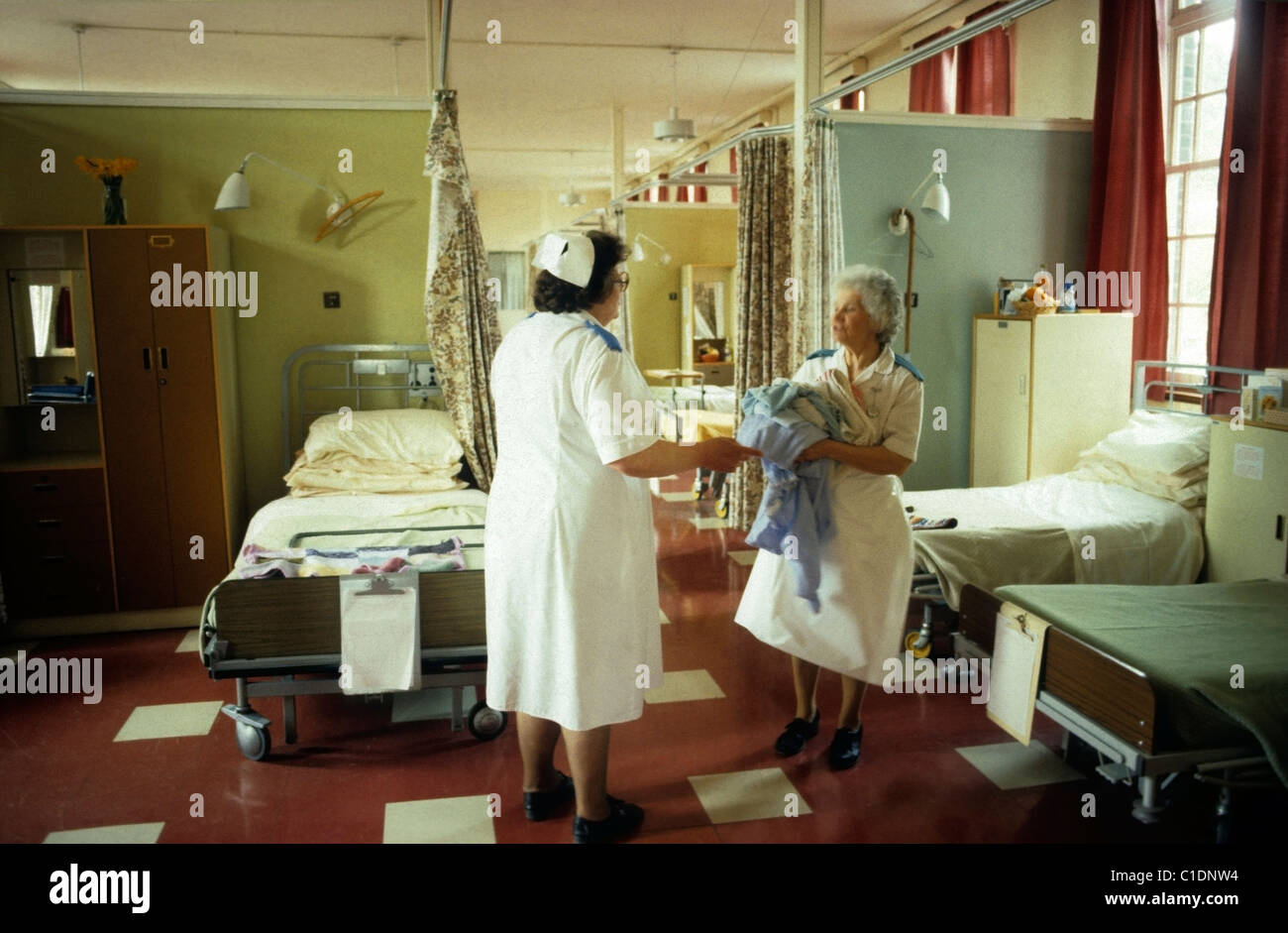 NHS nurse ward matron vintage nurses in a white uniforms in conversation changing linen on beds in  a geriatric ward  in a Bronglais hospital  in Aberystwyth Wales UK 1980s 1983   KATHY DEWITT Stock Photo