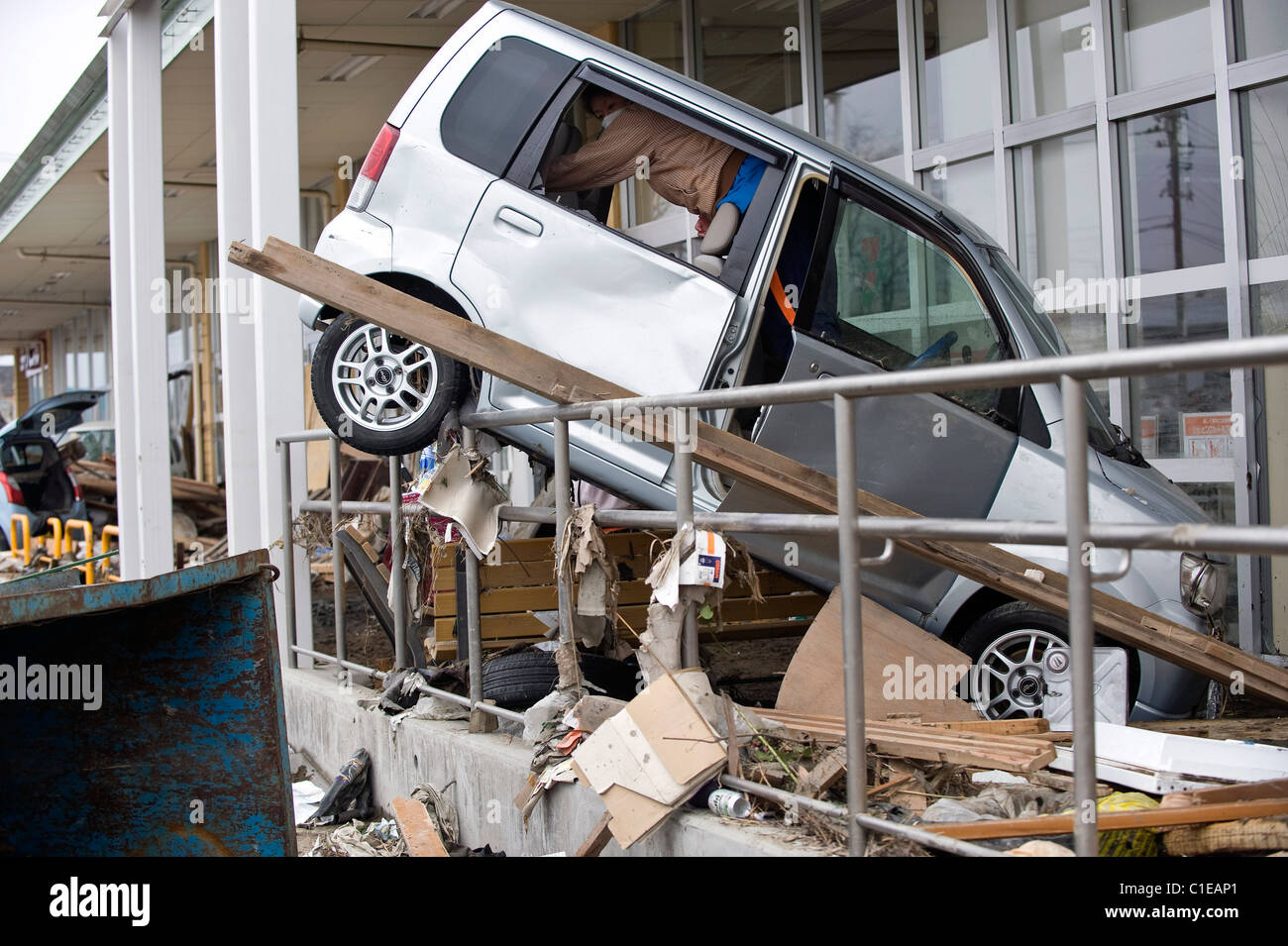 A man clears out his car that was forced over the barriers by the mega tsunami that followed the March 11 magnitude 9 quake Stock Photo