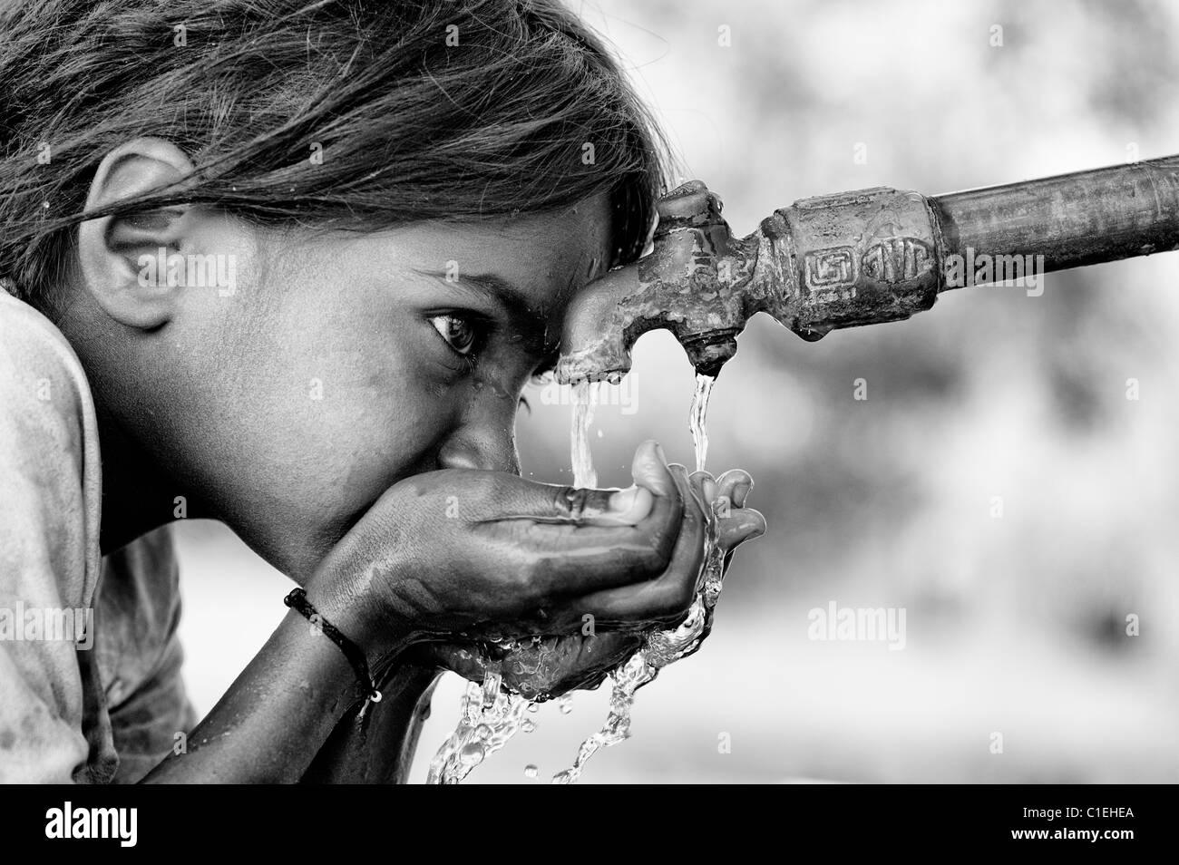 Young poor lower caste Indian girl drinking from a water tap. Andhra Pradesh, India. Monochrome Stock Photo