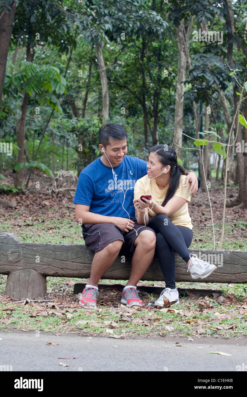 couple seated on a concrete park bench sharing smart phone Stock Photo ...