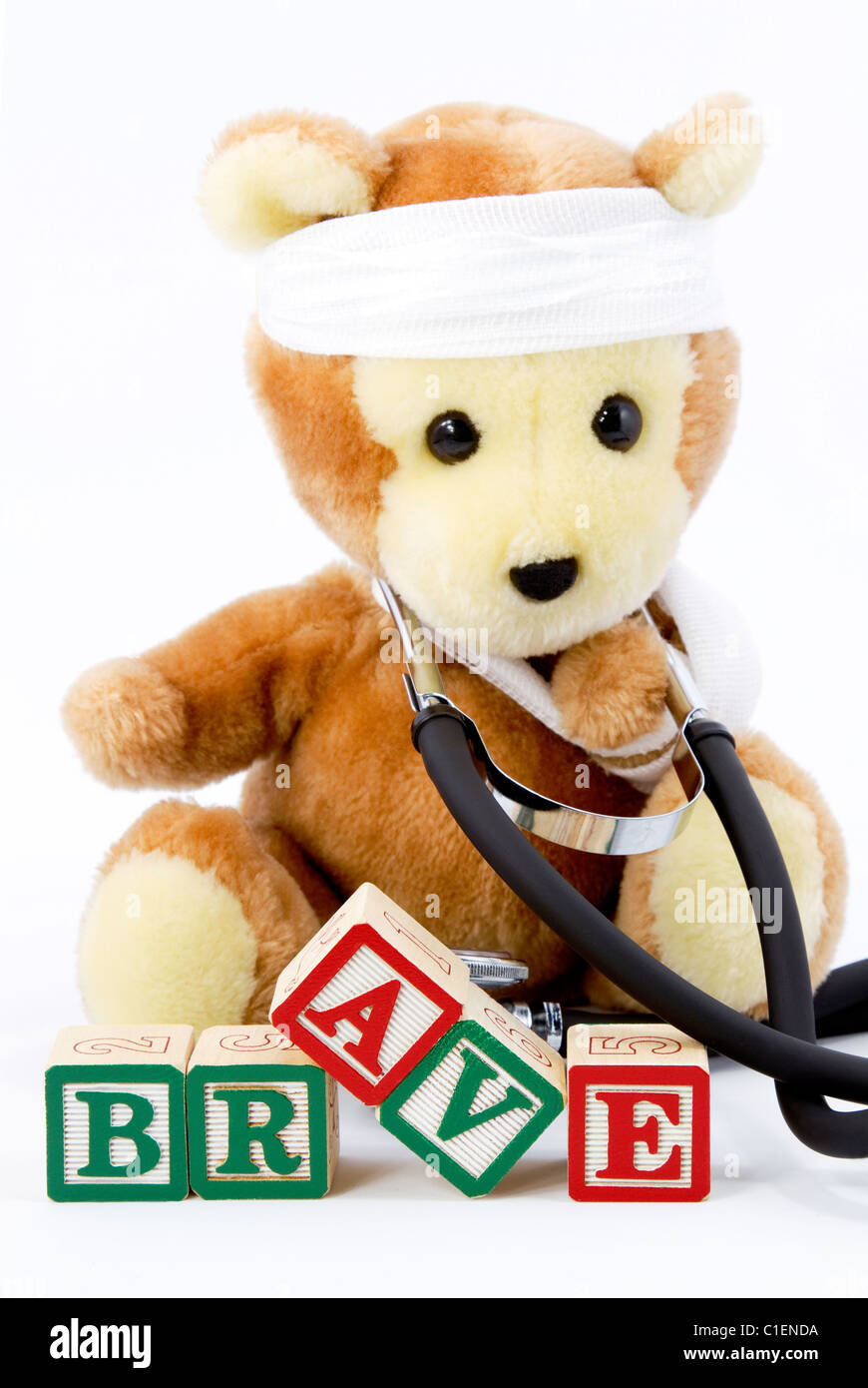 A stuffed bear wears a real stethoscope around its neck and sits behind blocks with BRAVE spelled out. Stock Photo