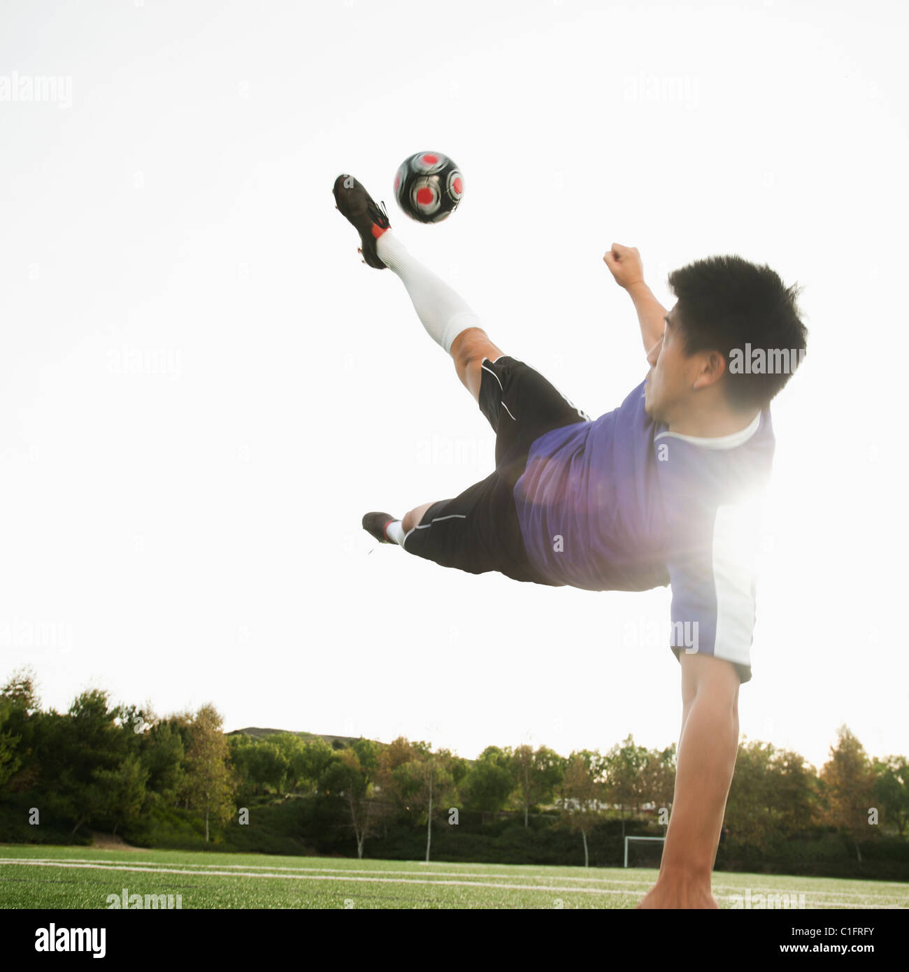 Asian soccer player in mid-air kicking soccer ball Stock Photo