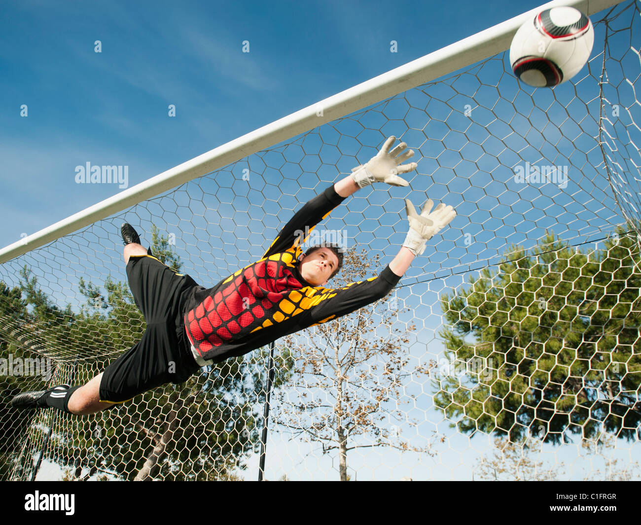 Mixed race goalkeeper in mid-air protecting goal Stock Photo