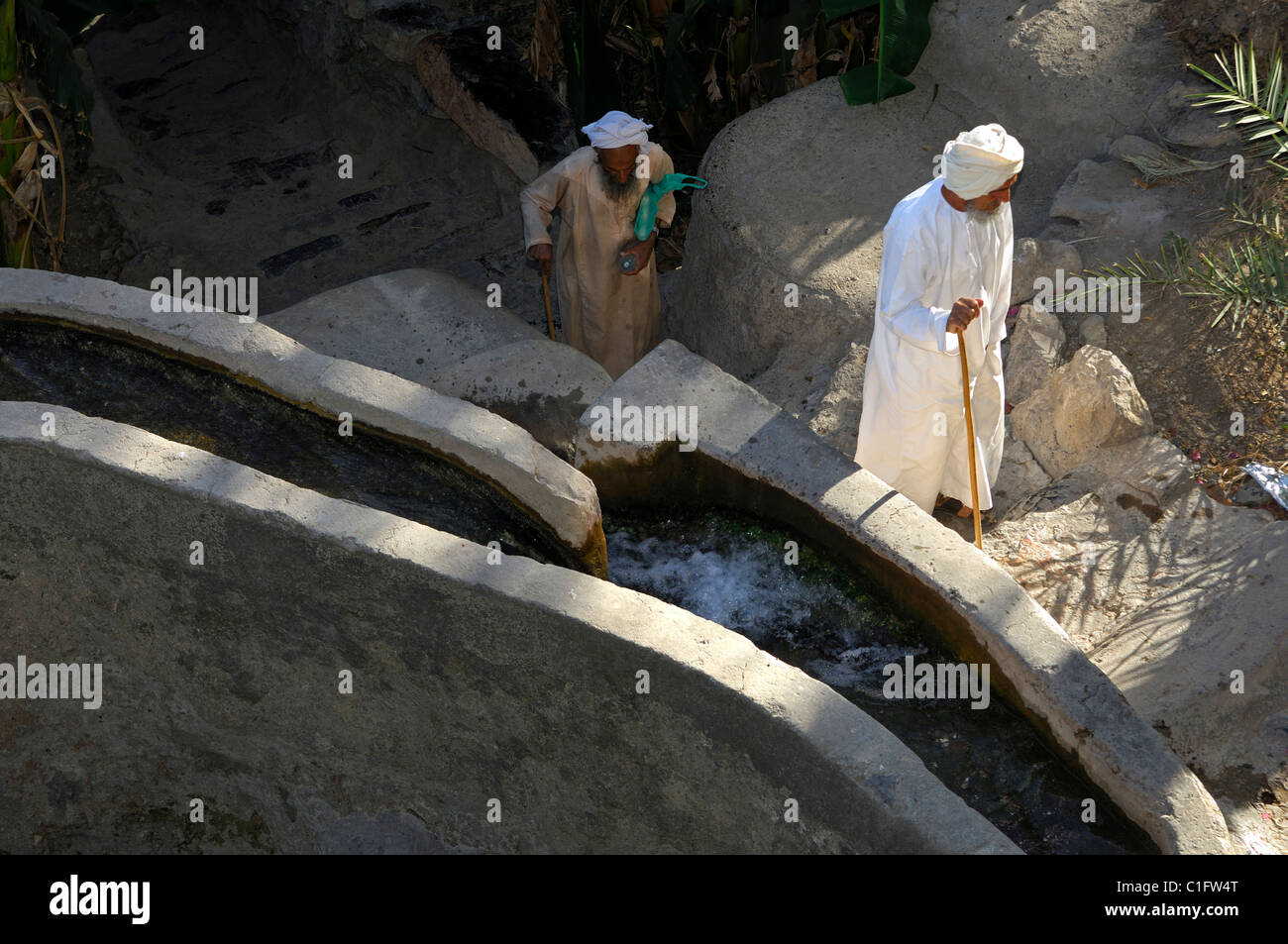 Elder Omani men in traditional clothing walking past an irrigation canal, Misfah al-Ibriyeen, Sultanate of Oman Stock Photo