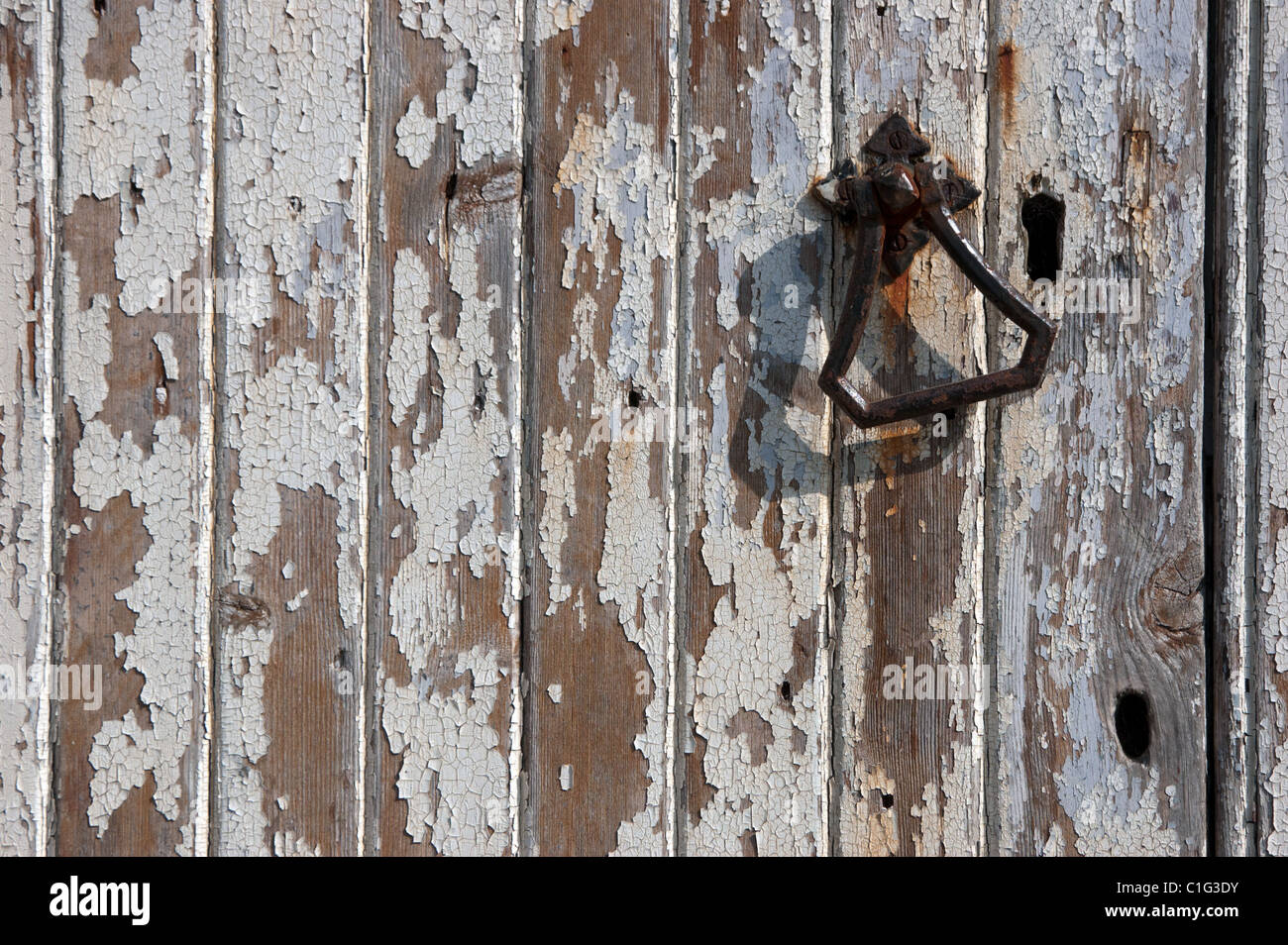 A weathered, painted chapel door with a metal handle. It's lit by angled sunlight giving an attractive shadow & texture. Stock Photo