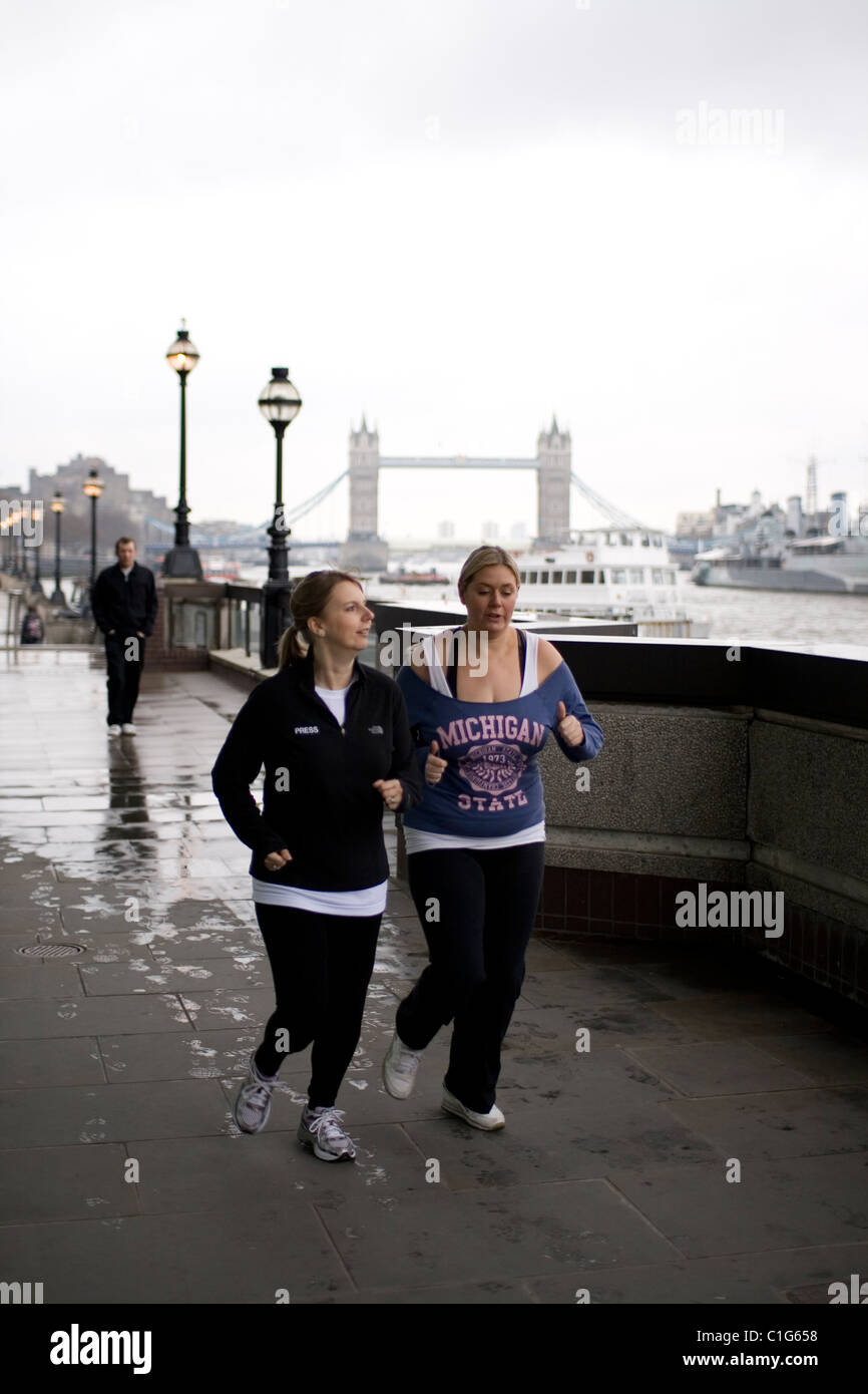 Two lunchtime joggers run along the footpath between London bridge and