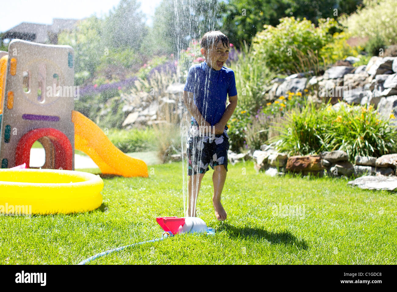 Caucasian boy playing in backyard sprinkler Stock Photo