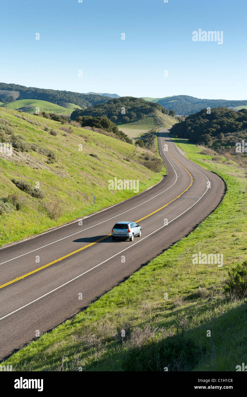 Car vehicle SUV automobile on highway winding through rolling hills covered with green grass and trees. California Highway 1. Stock Photo