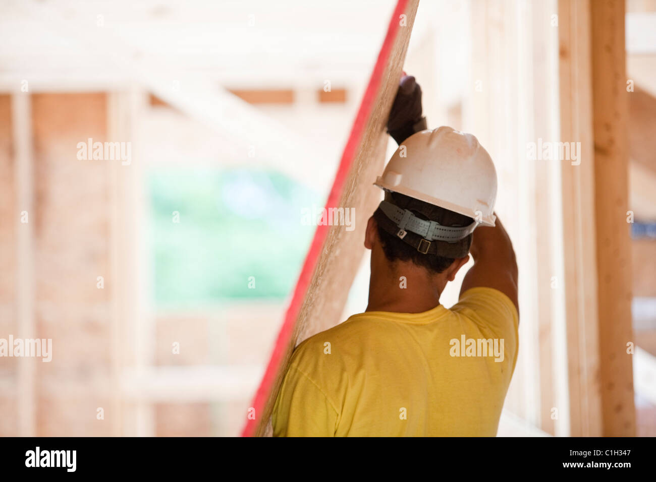 Hispanic carpenter carrying sheathing at a house under construction Stock Photo