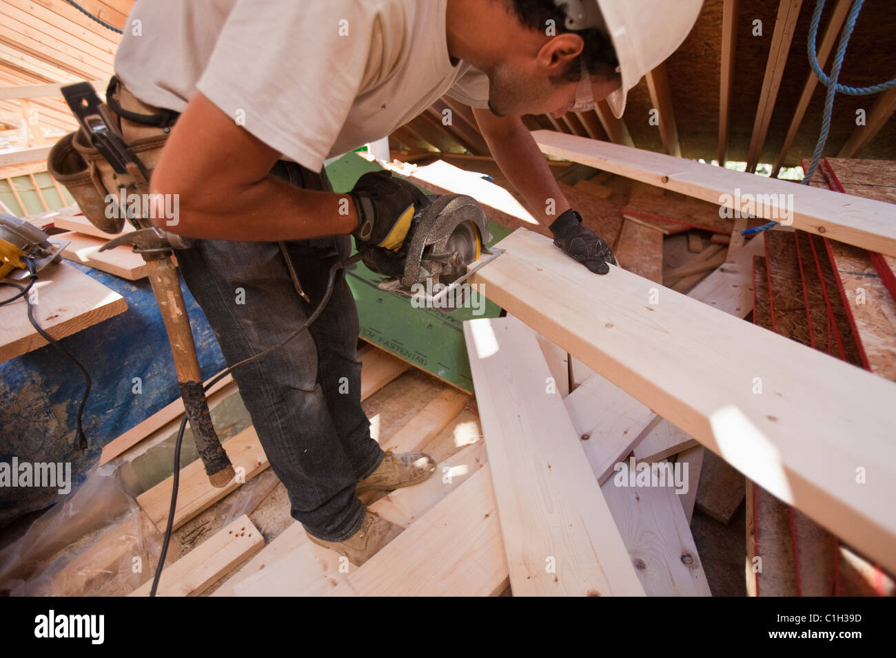 Hispanic carpenter using a circular saw at a  rafter at an angle house under construction Stock Photo