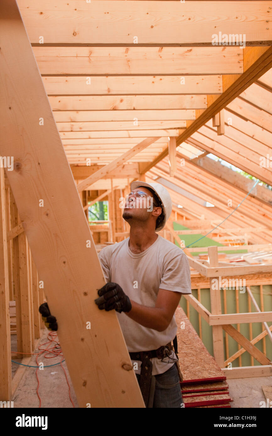 Hispanic carpenter passing up a rafter to roof at a house under construction Stock Photo
