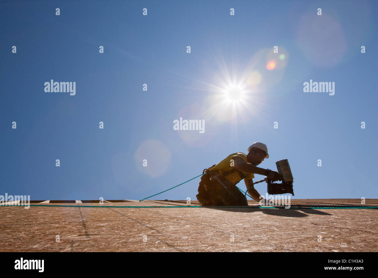 Hispanic carpenter using a nail gun on the roof of a house under construction Stock Photo