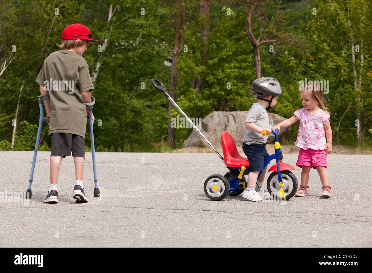 Boy with degenerative disease using crutches and a boy on tricycle with joint problems, little girl able bodied Stock Photo