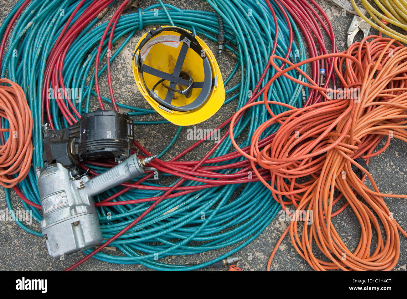 Closeup of power cords and air hoses with a nail gun and a hardhat at