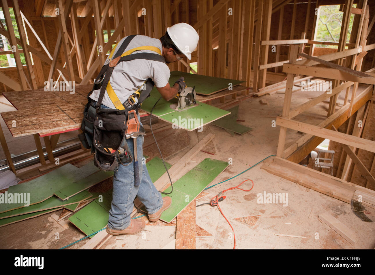 Carpenter using a circular saw on exterior wall sheathing in a house under construction Stock Photo